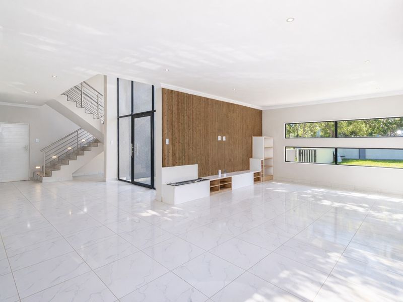 Spacious open-plan living area featuring modern porcelain tile flooring, a striking slatted timber feature wall, and a contemporary staircase with metal balustrades.