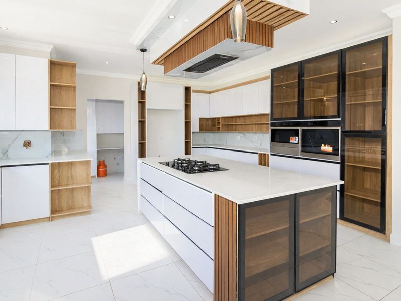 Modern kitchen featuring a central island with gas hob, high-end cabinetry, stone countertops, and integrated appliances in a bright, open-plan layout.
