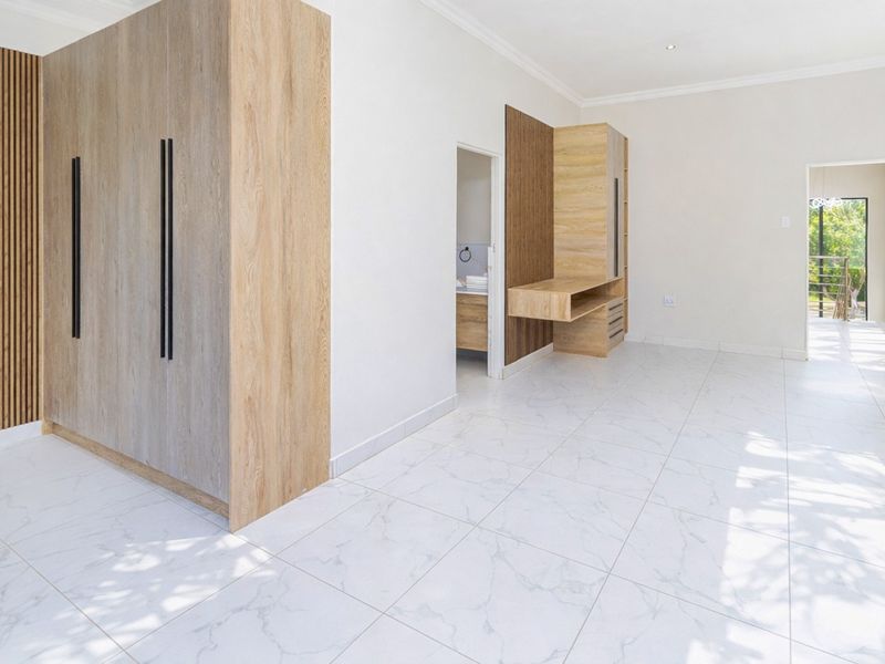 Modern bedroom featuring light wood built-in cabinetry, slatted wall accents, and polished marble-look floor tiles, with an adjoining en-suite bathroom.