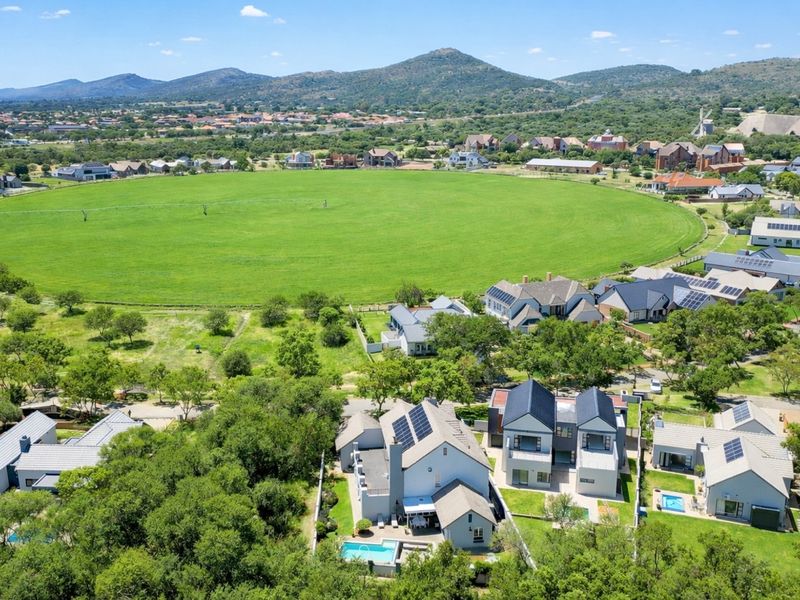 Aerial view of a residential estate featuring modern homes with solar panels, private swimming pools, and expansive green surroundings.