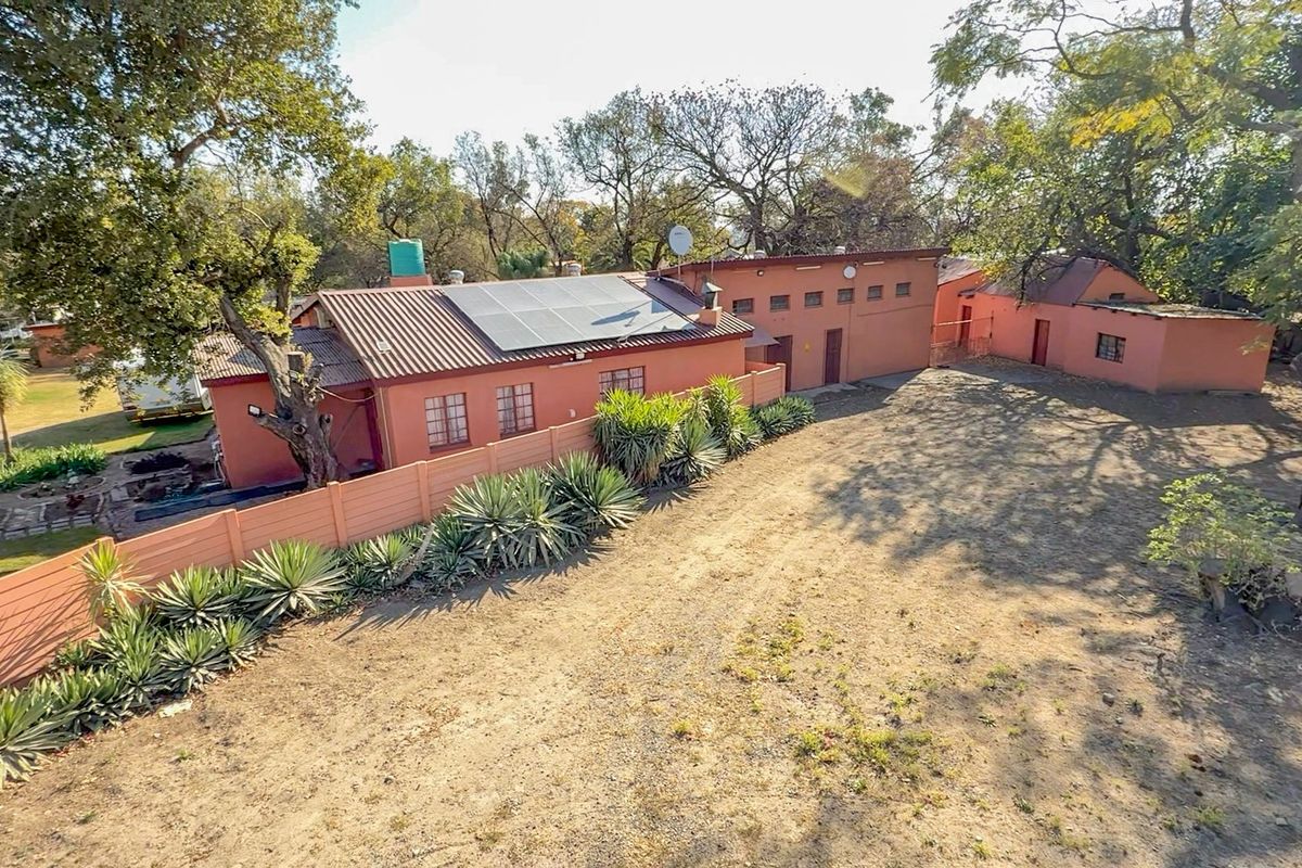 Aerial view of the small holding property featuring a main dwelling with solar panels, a large yard, and established trees.