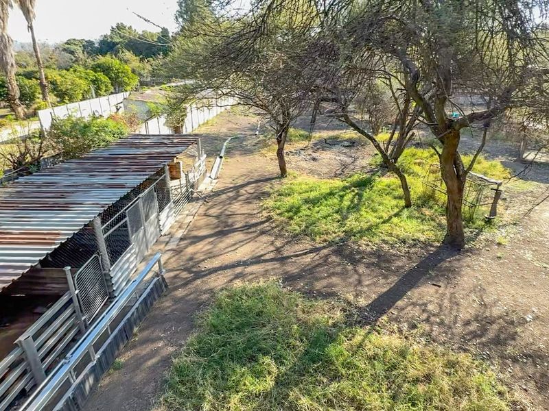 An elevated view of a large garden area featuring a corrugated iron structure, wire fencing, and established trees on a small holding property.