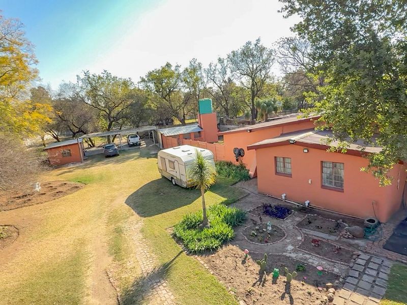 Aerial view of the small holding property featuring a main dwelling, carport, water tank, and established garden areas.
