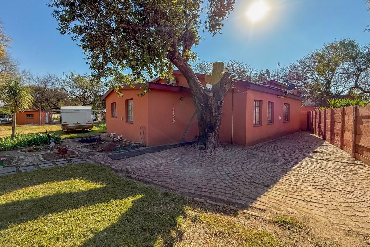 Rear view of the property featuring a terracotta-colored exterior, cobblestone paving, and a large mature tree within a fenced garden setting.