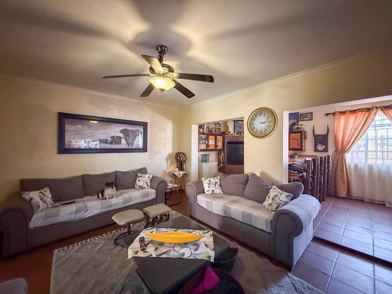 A living room featuring tiled flooring, a ceiling fan, and coved ceilings, with an open-plan layout leading to adjacent living spaces.
