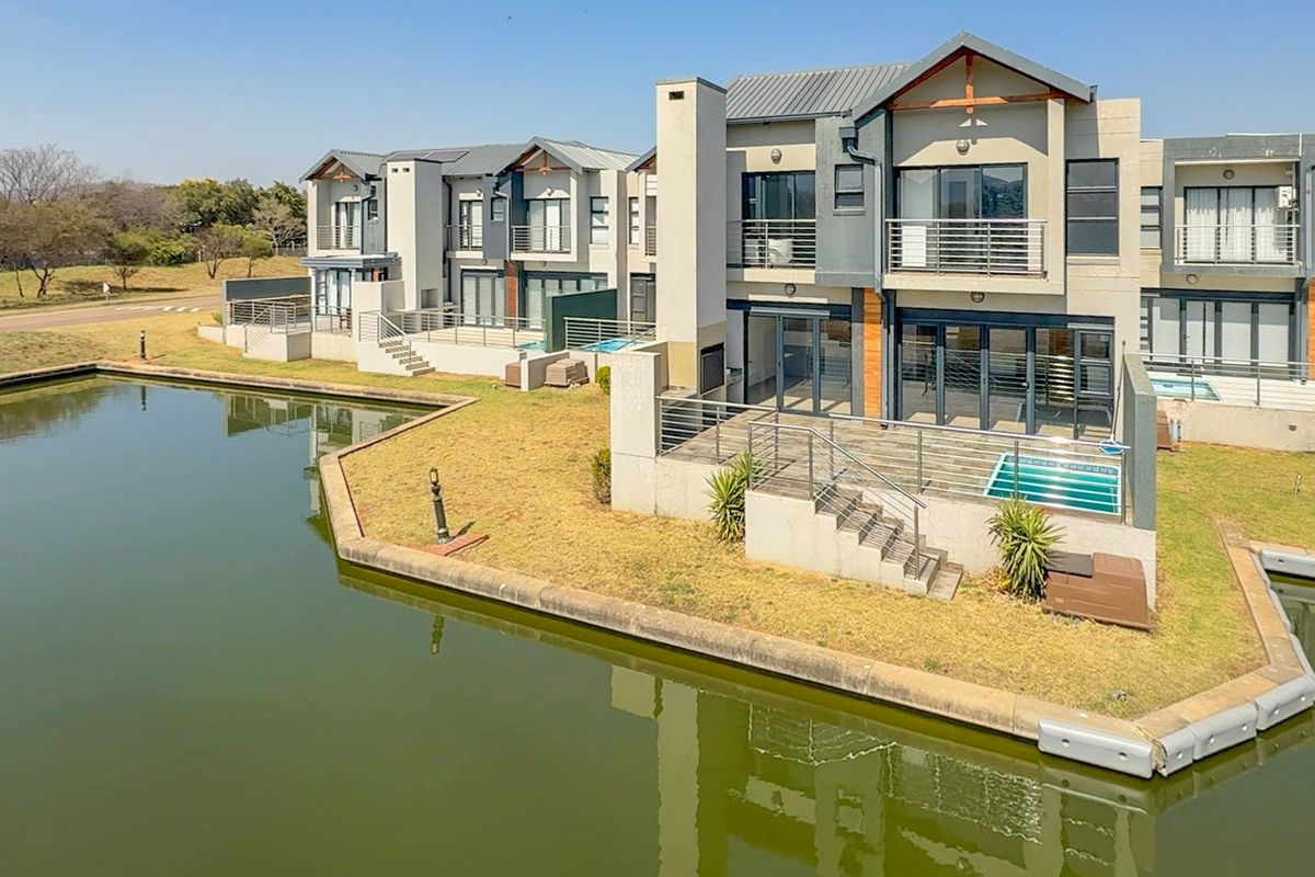 Rear view of a modern multi-story townhouse complex featuring private balconies, patios, and small plunge pools overlooking a waterfront canal.