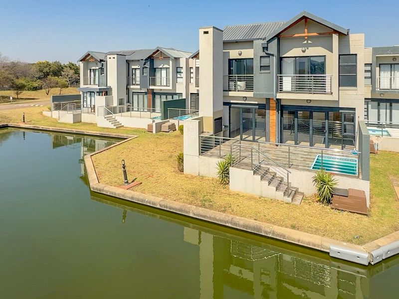 Rear view of a modern multi-story townhouse complex featuring private balconies, patios, and small plunge pools overlooking a waterfront canal.