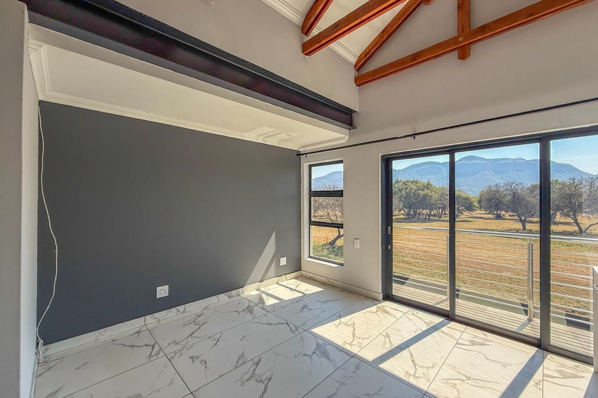 Bright living area featuring exposed timber trusses, modern marble-look floor tiles, and large sliding doors opening to scenic mountain views.
