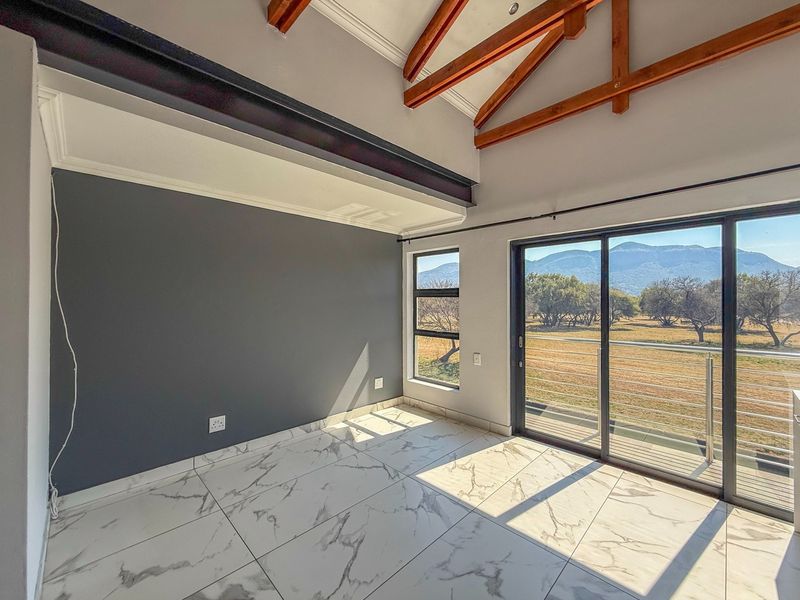 Bright living area featuring exposed timber trusses, modern marble-look floor tiles, and large sliding doors opening to scenic mountain views.