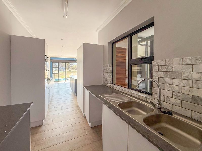 A clean, modern scullery featuring double stainless steel sinks, stone countertops, and marble-look subway tile backsplash with ample built-in cabinetry.