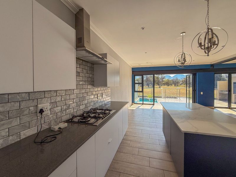 Modern open-plan kitchen featuring a gas hob, stone countertops, and a central island, flowing seamlessly through bi-fold doors to an outdoor pool area.