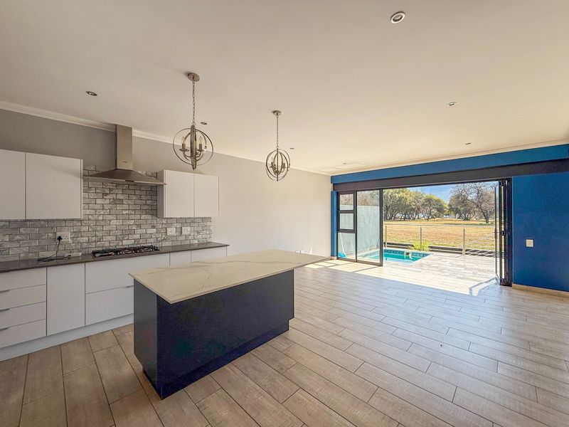 Modern open-plan kitchen and living area featuring a central island, gas hob, and large stacking doors opening to a patio and pool area.