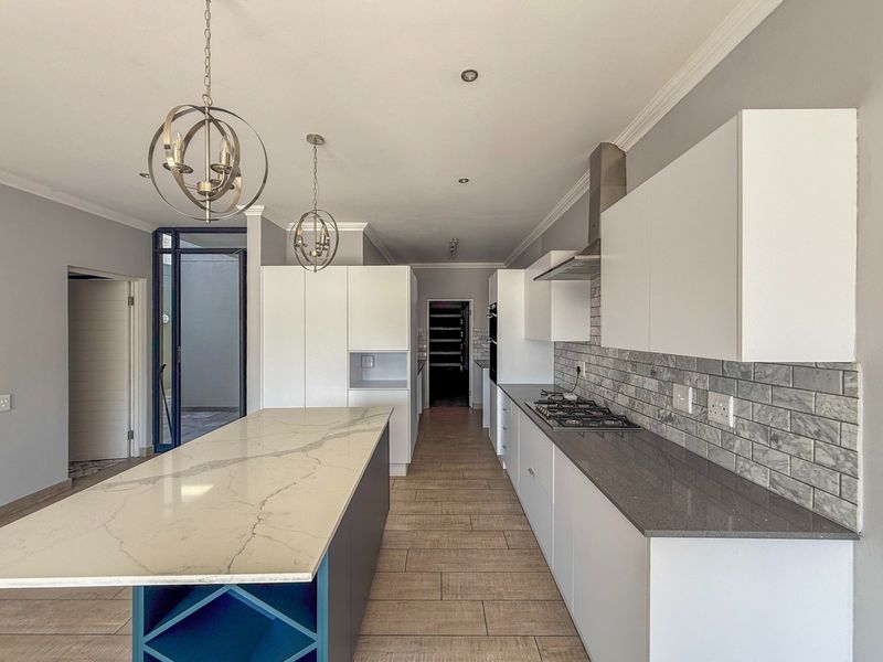 Modern kitchen featuring a large central island with stone countertops, gas hob, subway tile backsplash, and ample built-in cabinetry.