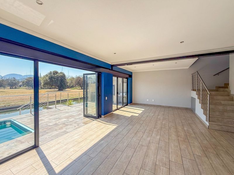 Spacious open-plan living area featuring large bi-fold doors opening to a patio, pool, and scenic views, with a modern staircase and tiled flooring.