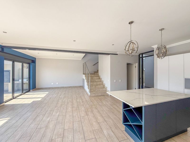 Spacious open-plan living area featuring a modern kitchen island with stone countertop, tiled flooring, and a staircase leading to the upper level.
