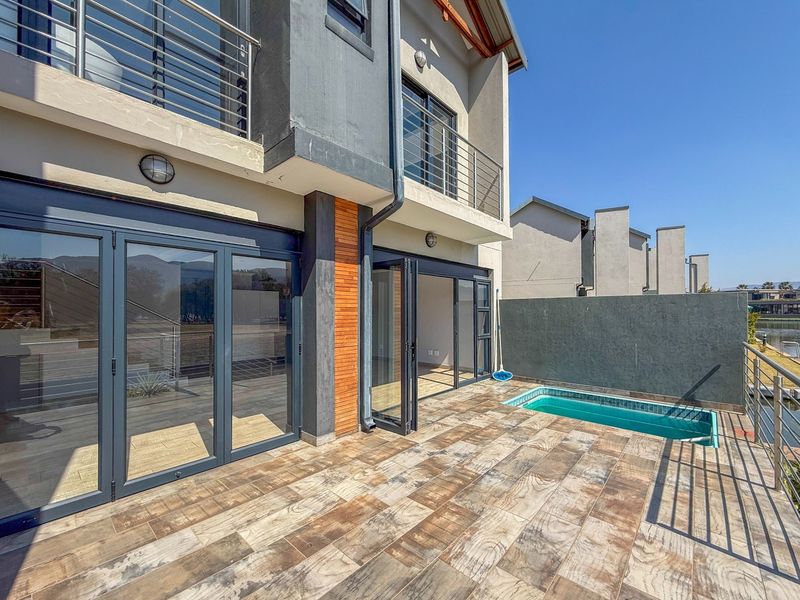 Rear exterior view featuring a tiled patio, a small swimming pool, and modern bi-fold doors leading into the home with upper-level balcony access.