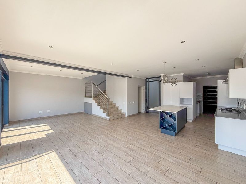Spacious open-plan living area featuring a modern kitchen with a central island, gas hob, and a staircase with a stainless steel balustrade.
