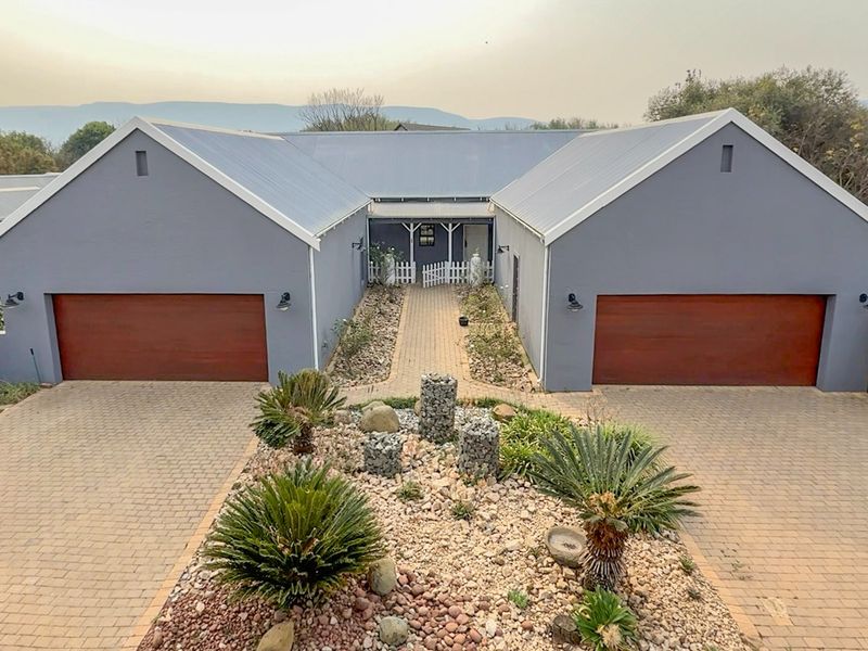Front elevation of a modern house featuring a double garage, paved driveway, and a well-maintained landscaped garden with gabion stone features.