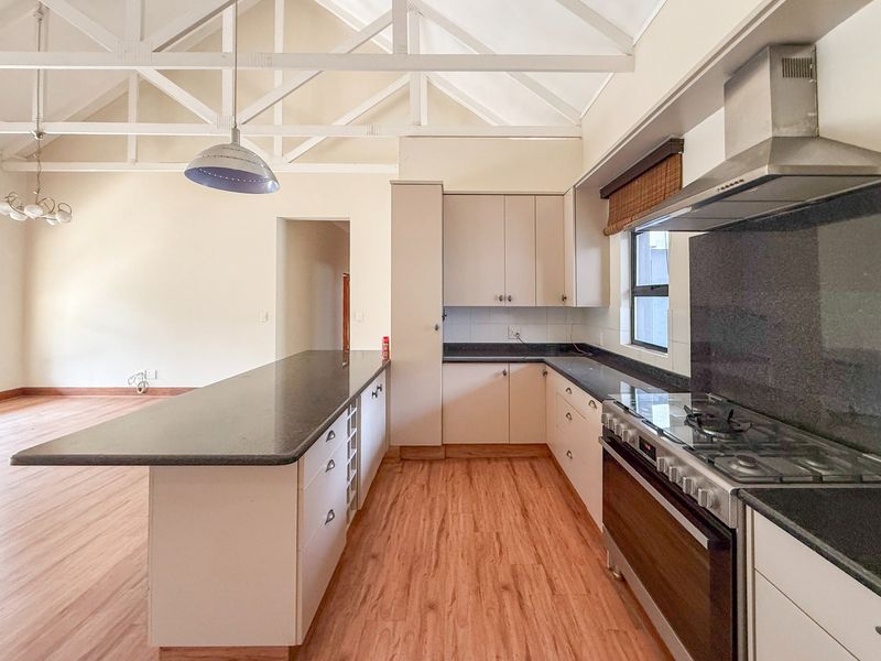 Spacious open-plan kitchen featuring vaulted ceilings with exposed trusses, granite countertops, a gas hob, and an integrated island, set against light-toned cabinetry.