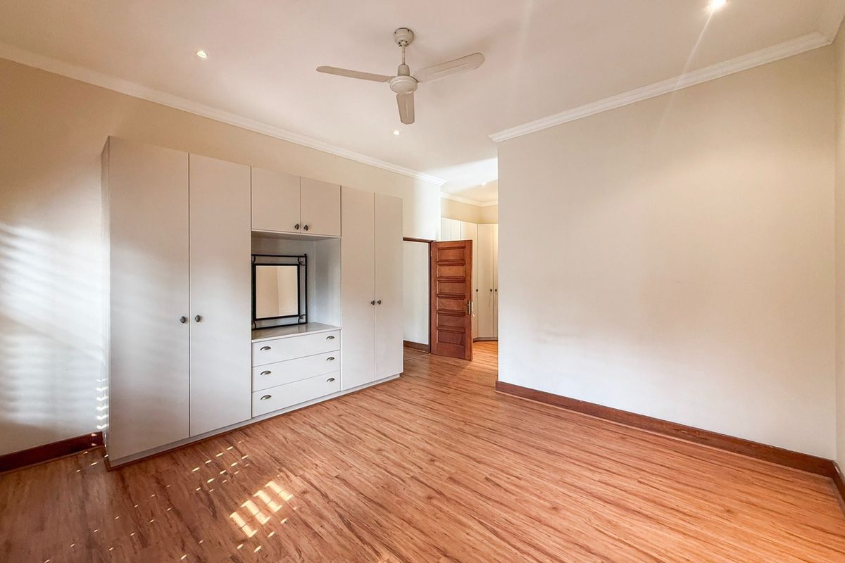 Spacious bedroom featuring light laminate flooring, extensive built-in cupboards with integrated vanity, ceiling fan, and recessed lighting.