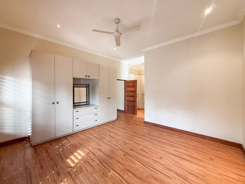 Spacious bedroom featuring light laminate flooring, extensive built-in cupboards with integrated vanity, ceiling fan, and recessed lighting.