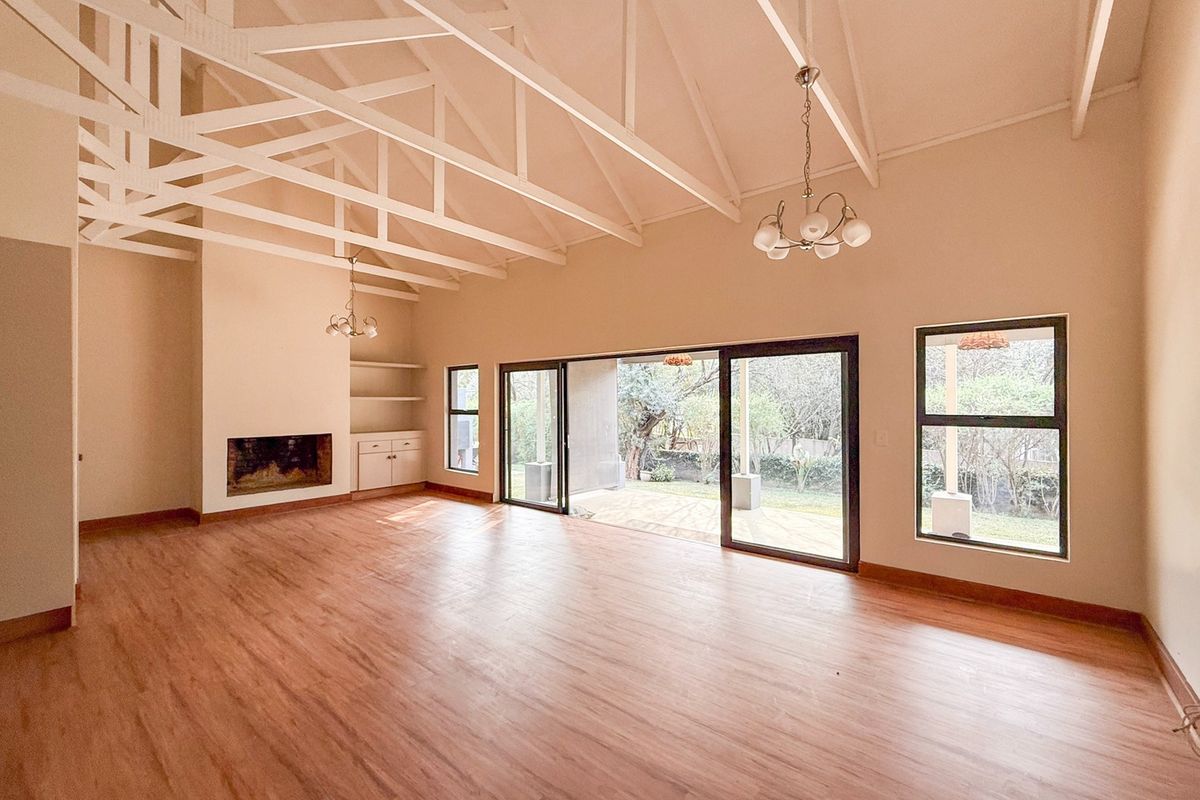 Spacious living room featuring a high vaulted ceiling with exposed trusses, built-in fireplace, and large sliding doors opening to the garden.