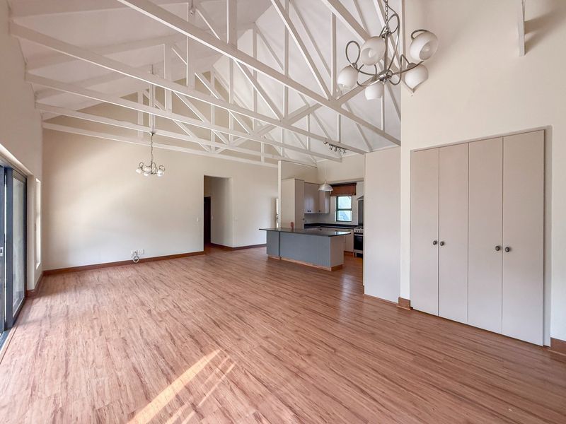 Spacious open-plan living area featuring high vaulted ceilings with exposed trusses, laminate flooring, and an integrated kitchen with a central island.