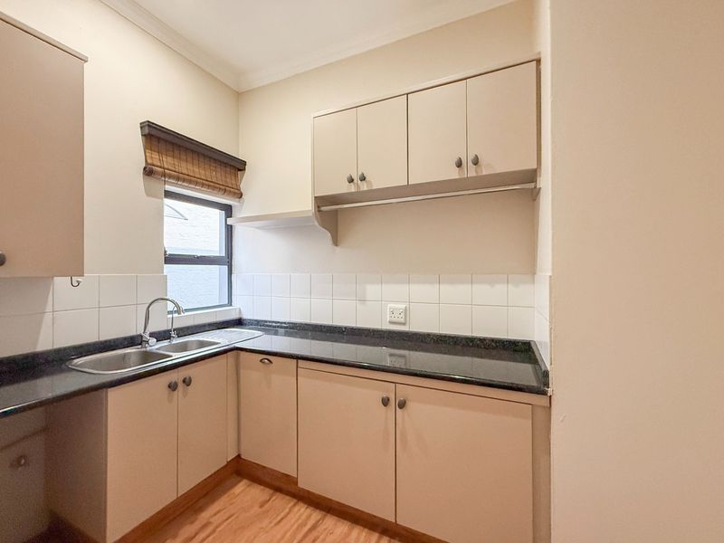 A clean and functional scullery featuring built-in cabinetry, laminate countertops, a double bowl stainless steel sink, and tiled splashbacks.