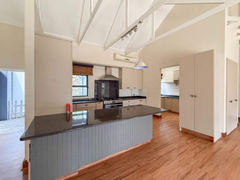 Spacious kitchen featuring a large island with granite countertops, gas stove, extractor fan, vaulted ceilings with exposed rafters, and an adjoining scullery area.