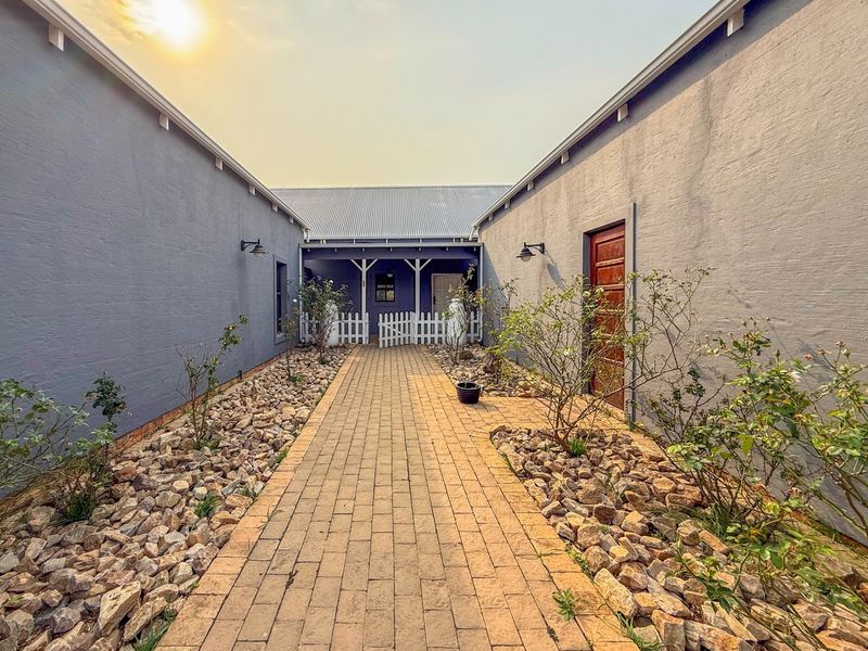 A well-maintained rear courtyard featuring a central paved walkway flanked by rock gardens, leading to a covered porch area with exterior lighting.