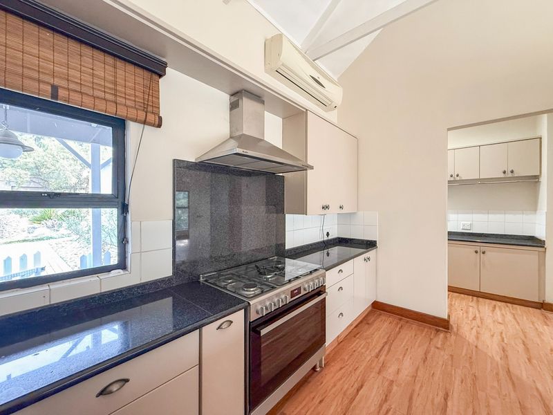A functional kitchen featuring granite countertops, a gas stove with extractor fan, and an adjoining scullery area with matching cabinetry.