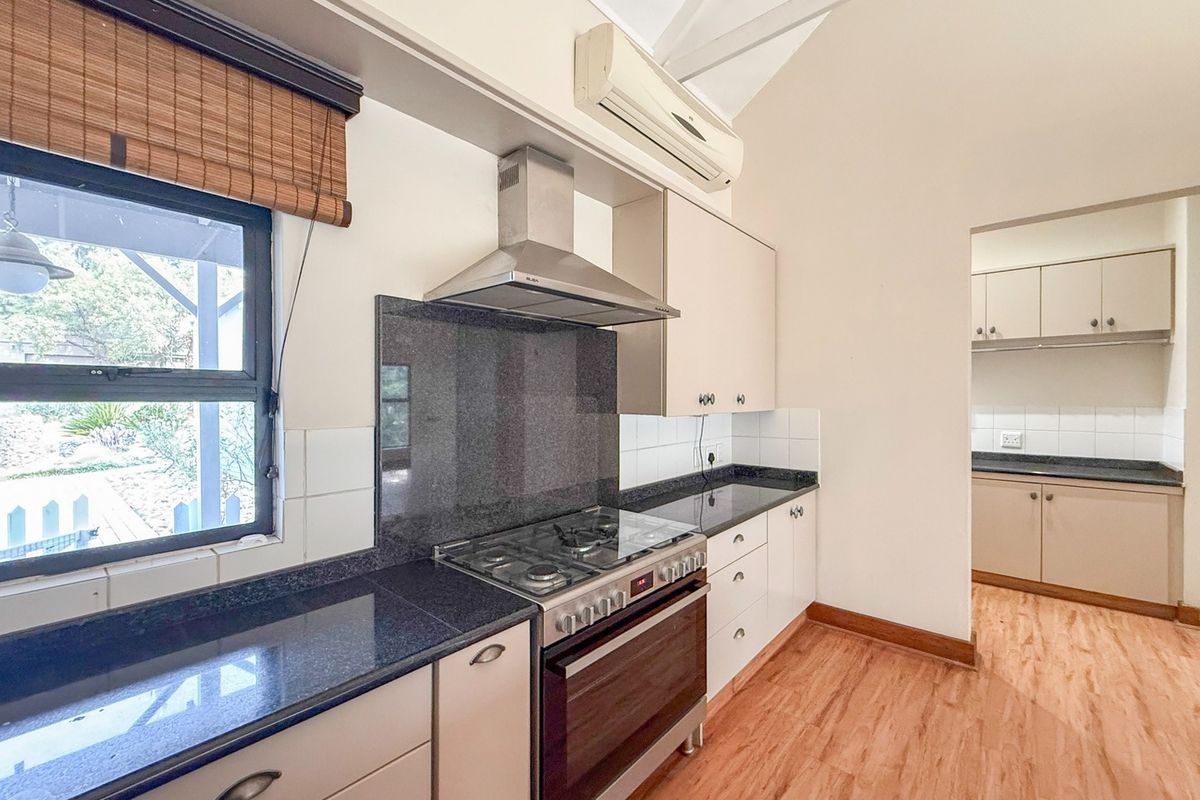 A functional kitchen featuring granite countertops, a gas stove with extractor fan, and an adjoining scullery area with matching cabinetry.