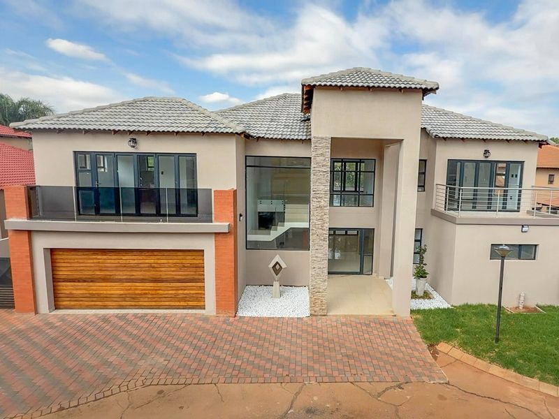 Modern double-storey residence featuring a timber garage door, stone cladding accents, glass balcony balustrades, and a paved driveway.