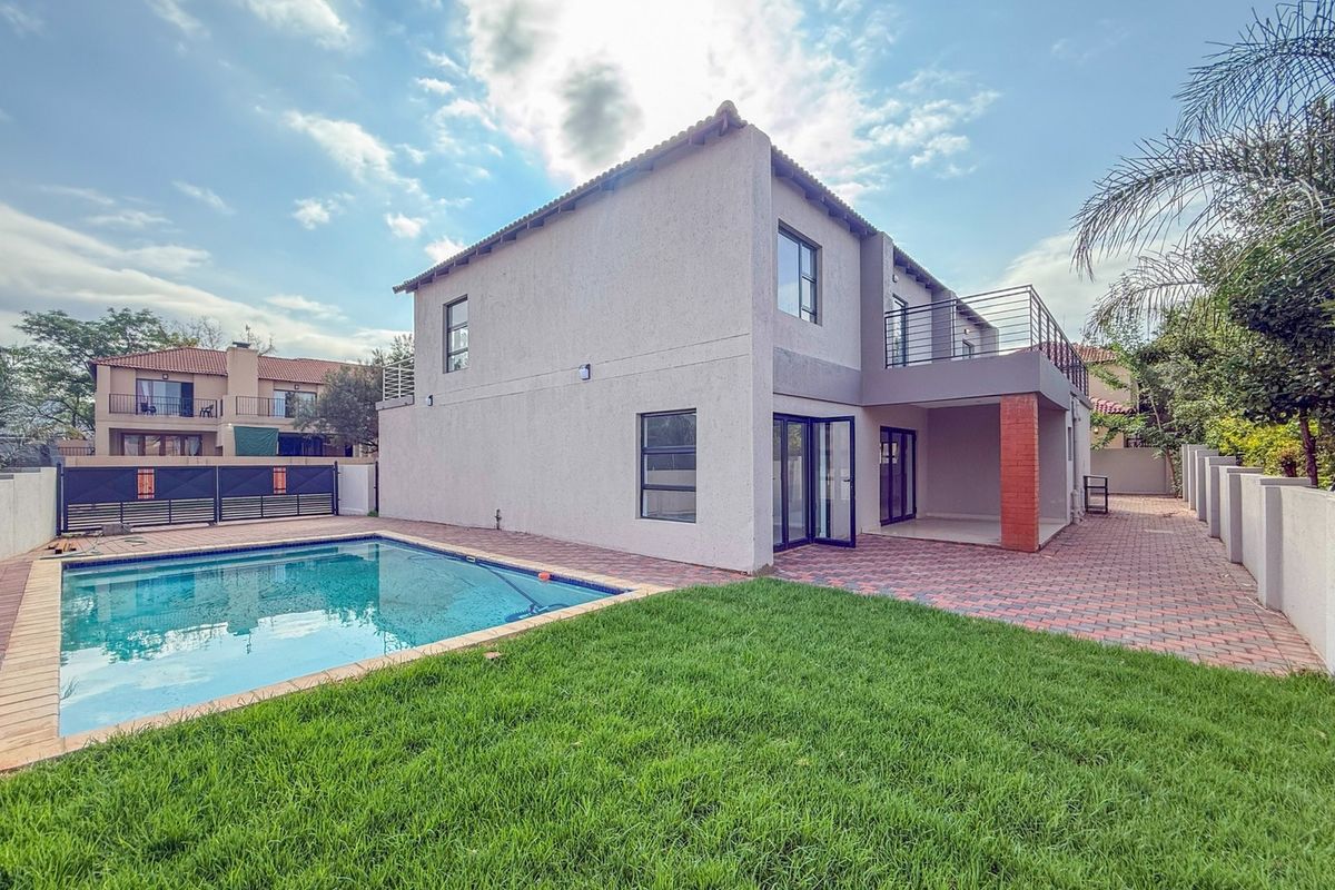 Rear view of the property featuring a swimming pool, paved patio area, and an upper-level balcony with metal railings.