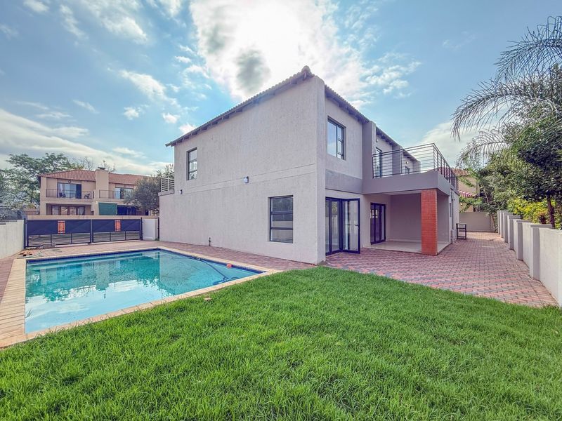 Rear view of the property featuring a swimming pool, paved patio area, and an upper-level balcony with metal railings.