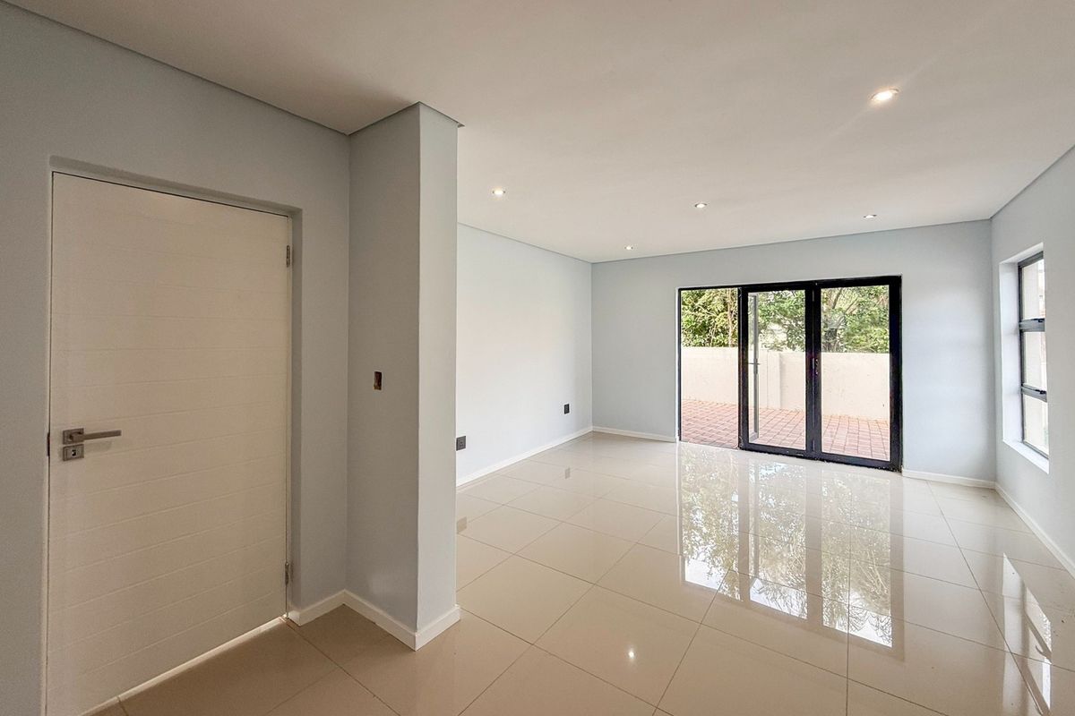 A bright, empty living area featuring polished tiled floors, recessed lighting, and large aluminium sliding doors providing access to an outdoor patio.