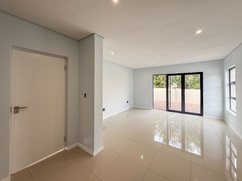 A bright, empty living area featuring polished tiled floors, recessed lighting, and large aluminium sliding doors providing access to an outdoor patio.