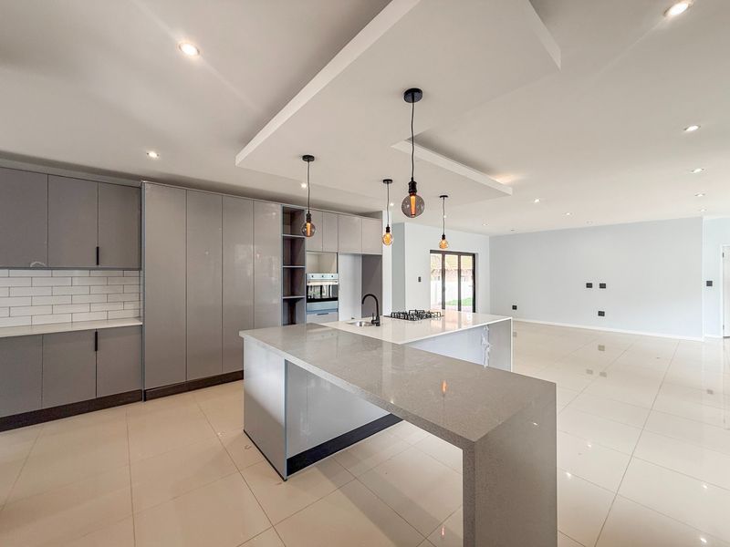 Modern open-plan kitchen and living area featuring a large island with quartz countertops, built-in appliances, and sleek grey cabinetry with recessed lighting.