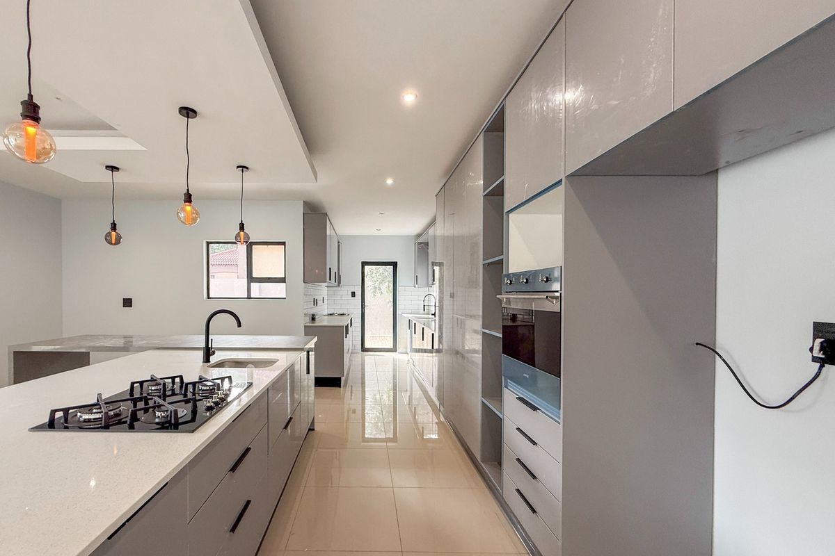 Modern kitchen featuring sleek grey cabinetry, quartz countertops, a gas hob, built-in oven, and polished tiled flooring in an open-plan layout.