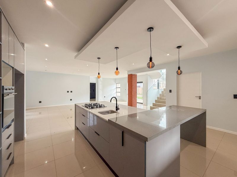 Modern open-plan kitchen featuring a large island with gas hob, sleek cabinetry, and integrated appliances, flowing into a spacious living area with staircase access.