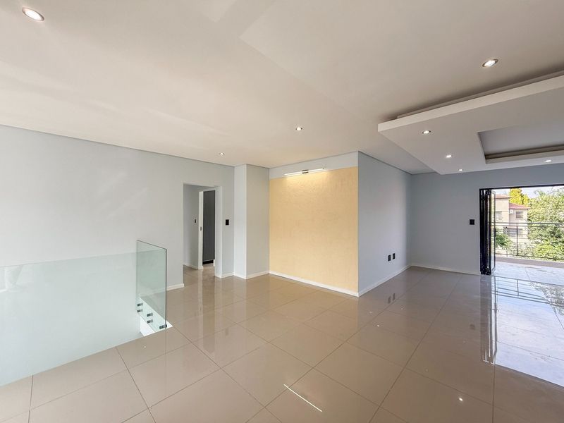 Spacious, modern open-plan living area featuring polished porcelain tiles, recessed downlighting, a decorative ceiling bulkhead, and a glass balustrade overlooking the staircase.