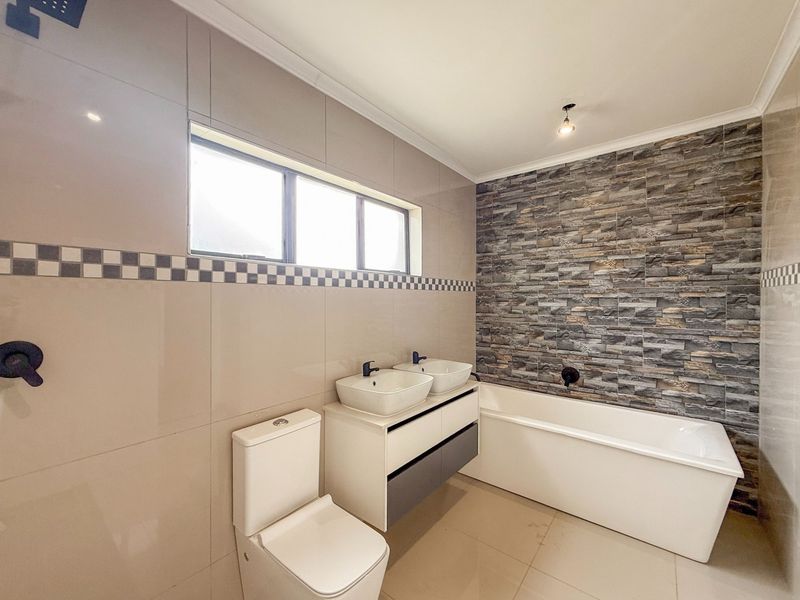 Modern bathroom featuring a double vanity, built-in bathtub, toilet, and a striking stone feature wall with contemporary fixtures.