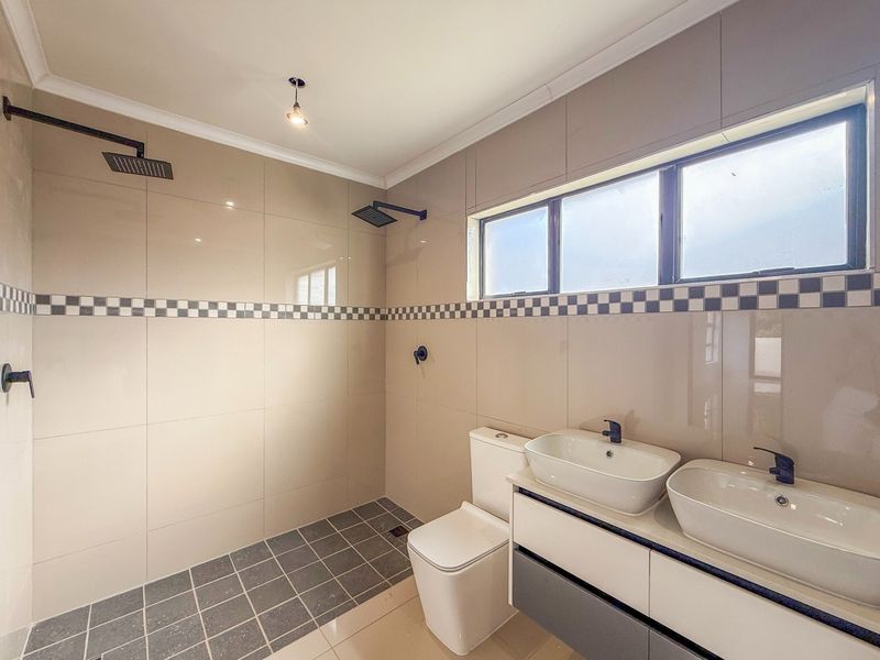 Modern bathroom featuring a double vanity, dual shower heads in a walk-in shower, and neutral tiled finishes.