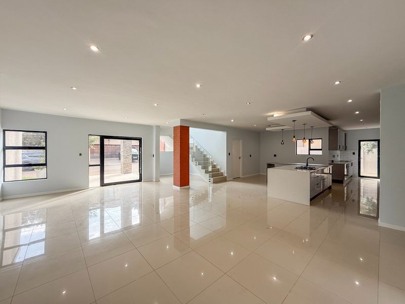 Spacious open-plan living and kitchen area featuring polished floor tiles, a modern kitchen island with gas cooktop, and a feature staircase.