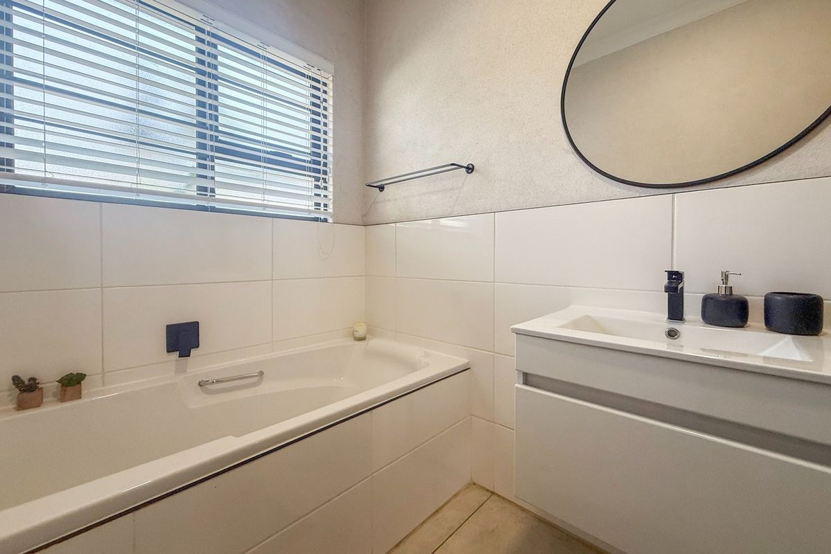Modern bathroom featuring a built-in bathtub, sleek vanity cabinet with basin, contemporary mixer tap, and a wall-mounted mirror.
