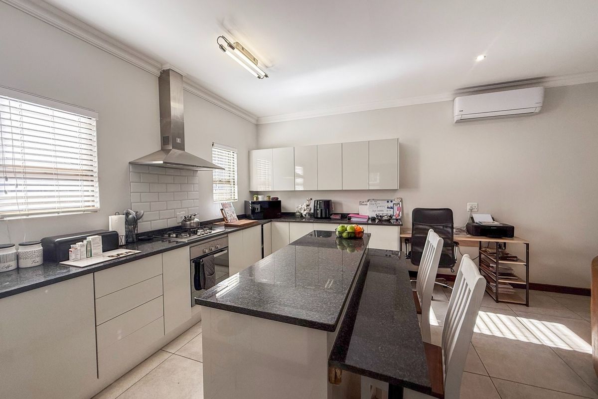 Modern kitchen featuring granite countertops, a central island, built-in oven with gas hob, stainless steel extractor, and tiled flooring.