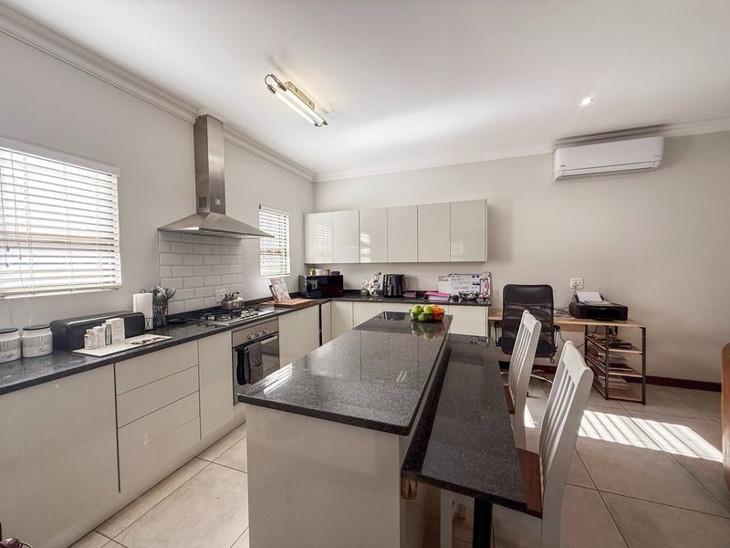 Modern kitchen featuring granite countertops, a central island, built-in oven with gas hob, stainless steel extractor, and tiled flooring.