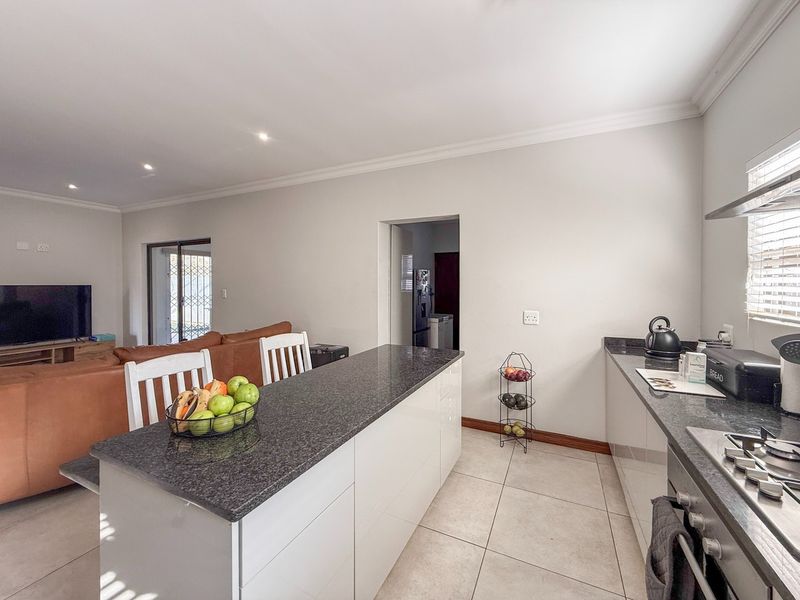 Modern open-plan kitchen featuring granite countertops, sleek cabinetry, and a gas hob, seamlessly flowing into the adjacent living area with tiled flooring throughout.