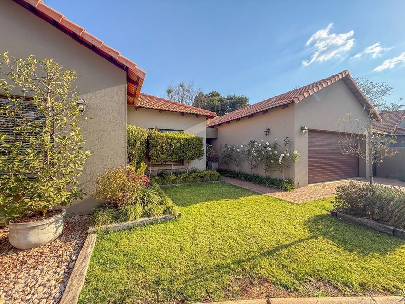 Front view of the house featuring a well-maintained garden, paved driveway, and a single garage with a tiled roof.