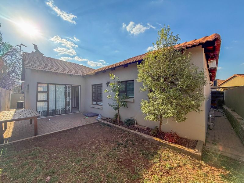 Rear view of the house featuring a paved patio area, sliding glass doors with security gates, and a garden with a retaining wall.